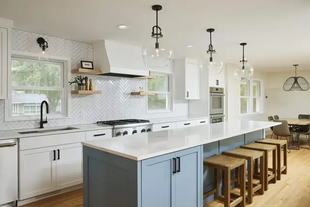 Kitchen with white shaker cabinets, a pale blue island with wood stools, herringbone tile backsplash and glass globe pendants