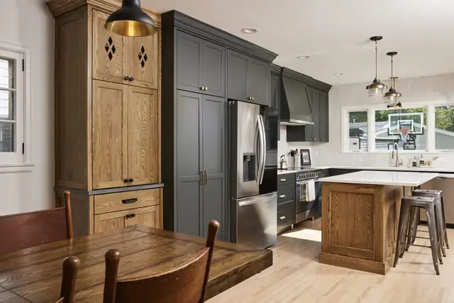 Kitchen with charcoal and stained oak cabinetry, a wood island with stools, black pendants and a stainless refrigerator