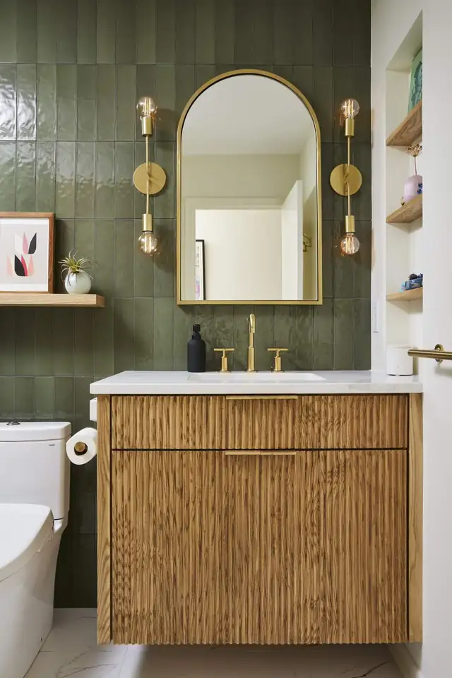 Bathroom with olive green vertical tile, a fluted wood floating vanity, brass sconces and an arched mirror