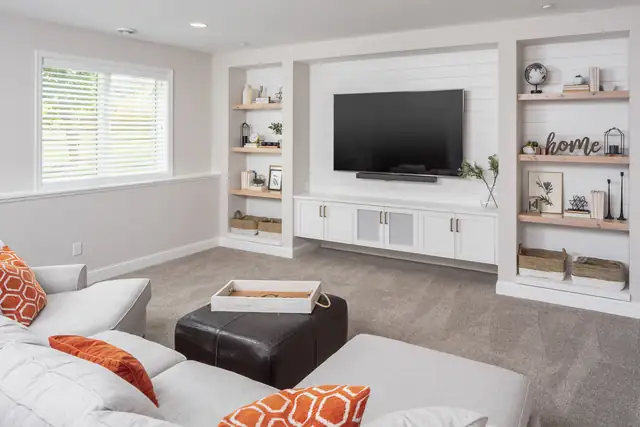 Finished basement family room with a white built-in TV wall, open shelving and a sectional sofa