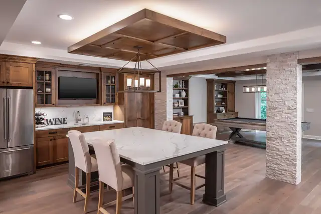 Finished basement with a quartz-topped game table, coffered wood ceiling, built-in TV wall and wine bar