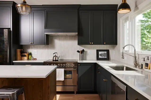 Kitchen with black shaker cabinets, white quartz counters, a stainless range and brass pendant lights