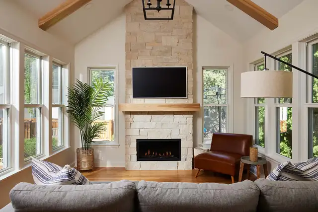 Four-season porch with a vaulted ceiling, a limestone fireplace, a cognac leather chair and windows on three sides